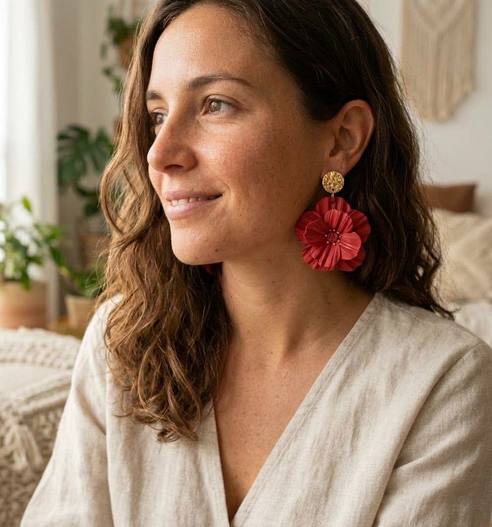 Imagen hecha con IA: mujer sonriendo con un arete de flor roja Aura Floral de pétalos texturizados colgado de un topo dorado martillado